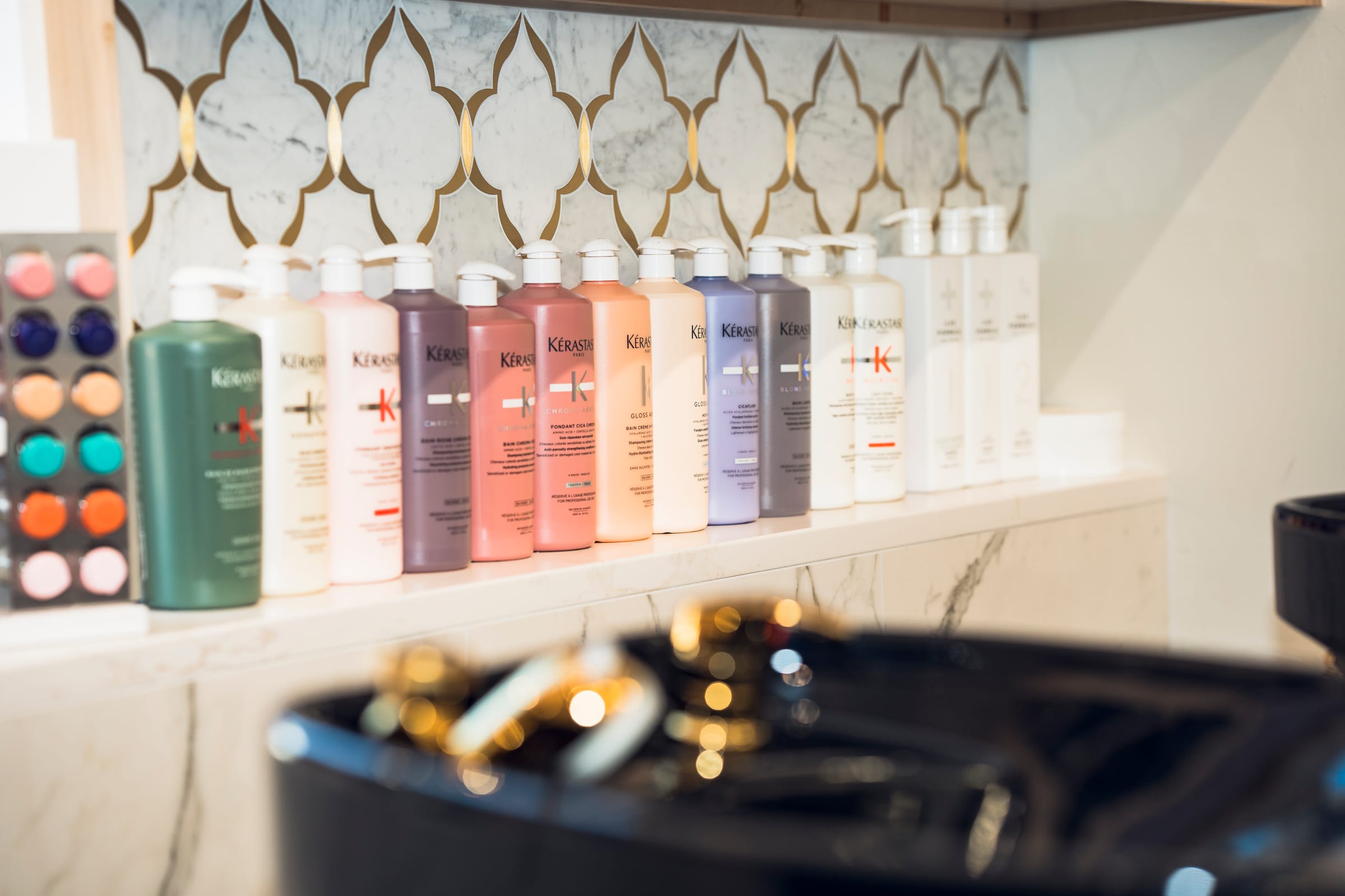 Kérastase liter bottles lined on the marble backbar over the black basin