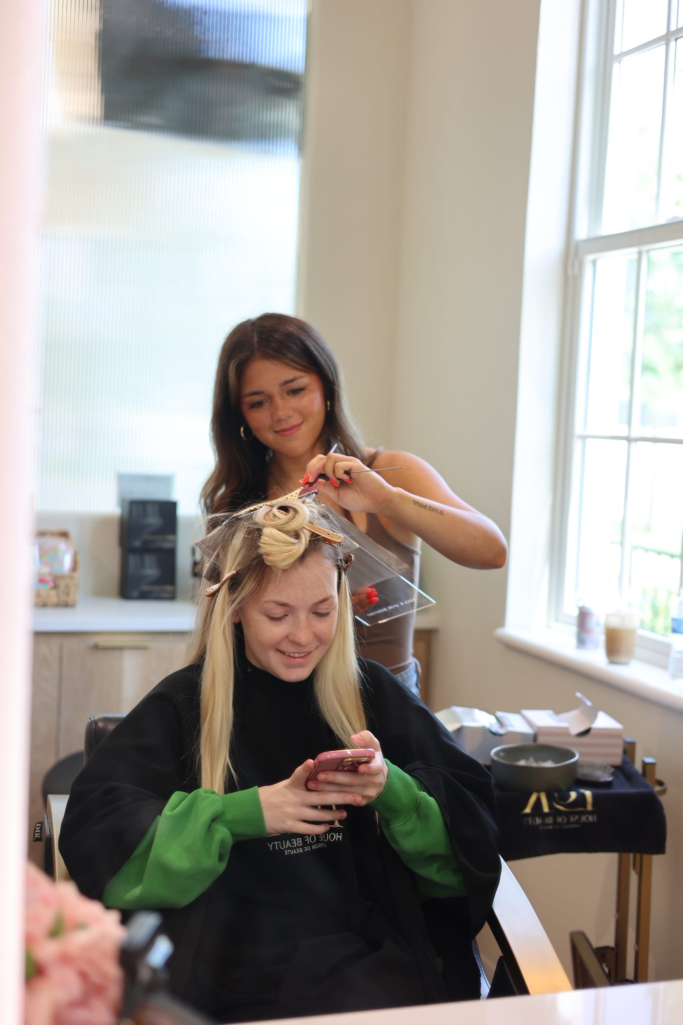 Foils and toner painted in by the window while the guest scrolls her phone under the cape