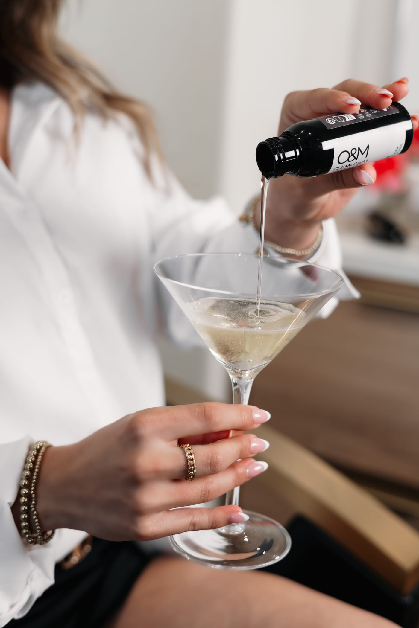 A martini being poured into a coupe glass at the chair, rings and bracelets catching the light
