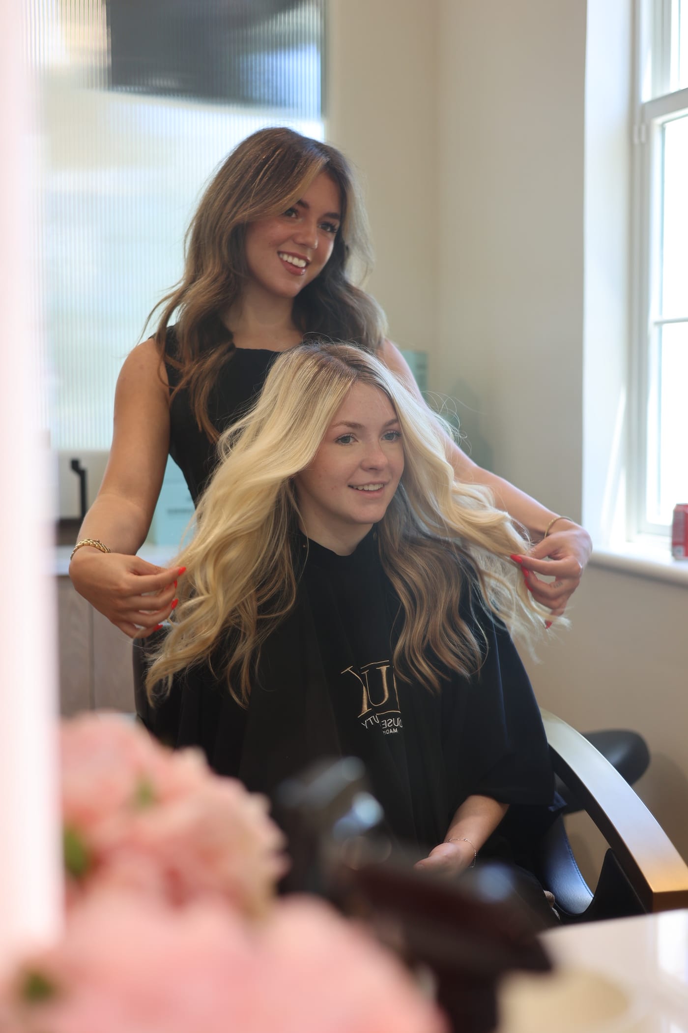 Stylist and guest laughing mid-blowout, fresh blonde lengths catching the light
