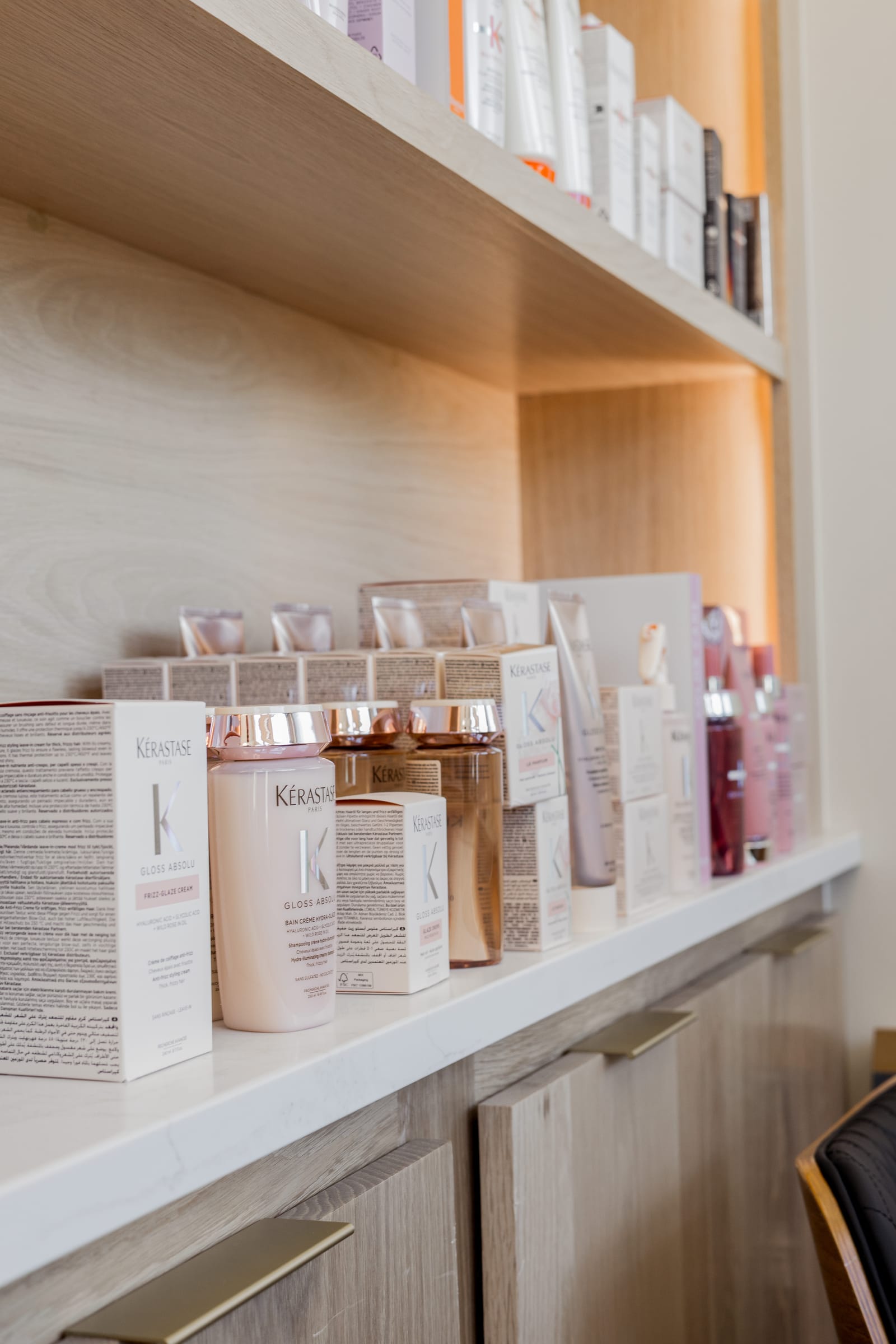 Kérastase Gloss Absolu bottles and boxes lined up on the oak shelf at LŪK